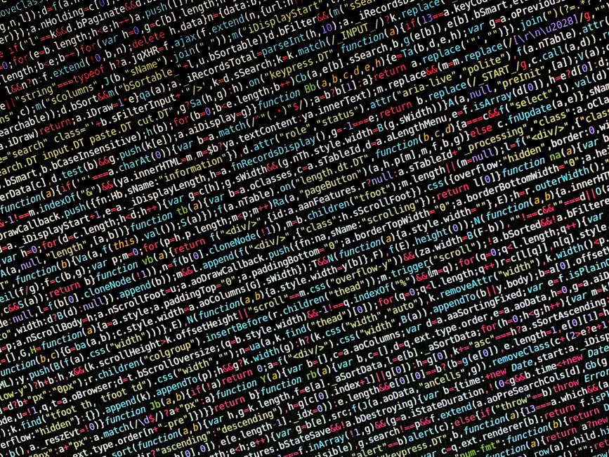A person’s hands typing on a sleek, open laptop with a dark-themed code editor on the screen, displaying lines of coloured programming code. The laptop is placed on a dark, reflective surface, possi