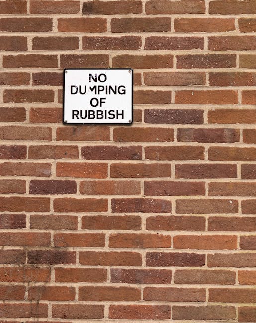 Two large black bagged waste bundles are positioned on the edge of a paved street, leaning slightly against a black metal fence with vertical bars. The bags appear to contain mixed rubbish, with some